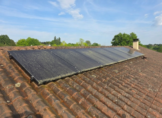 Panneaux solaires installés sur un toit avec ciel bleu et arbres en arrière-plan.
